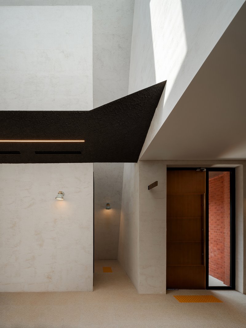 Interior hallway with white plaster walls and black ceiling plane beside open doorway