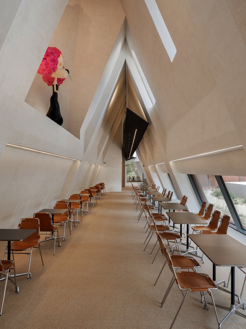 Interior view of a tall angular chapel with rows of orange chairs and a red artwork suspended overhead