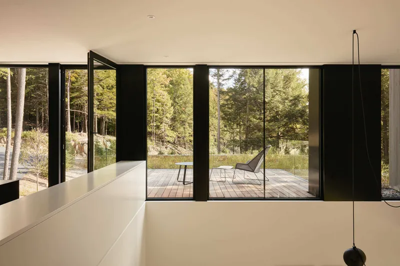 Black-framed sliding doors opening from upper level to a timber deck among the trees