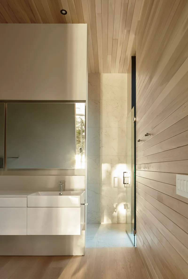 Bathroom vanity beside a narrow glazed slot framing sunlight and trees beyond