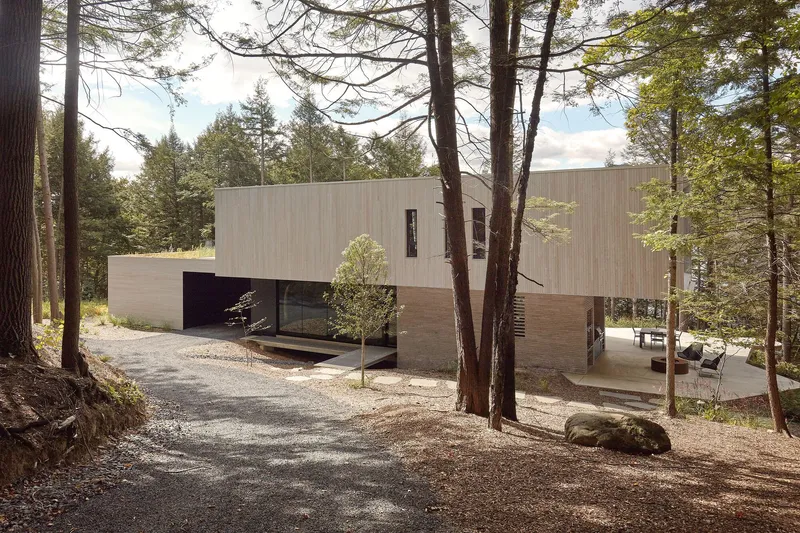 Cantilevered upper volume clad in pale wood above a recessed lower floor and gravel driveway
