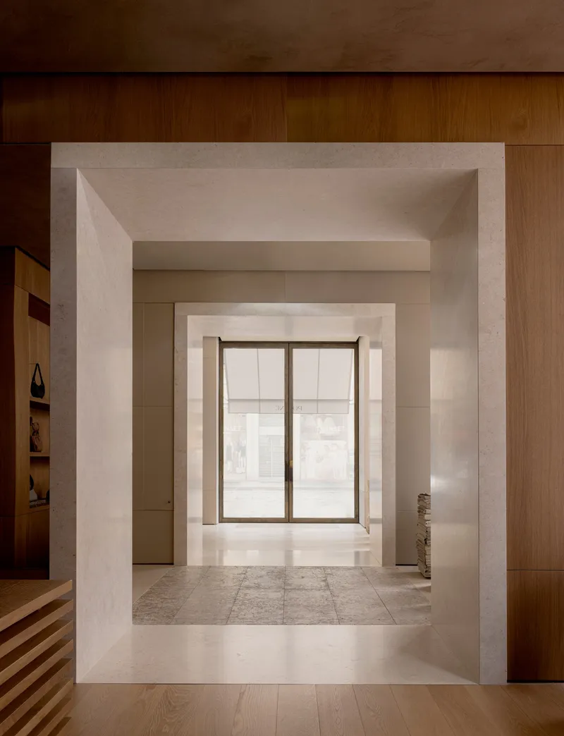Enfilade of stone portals framing a glazed entrance at the far end under linear ceiling lighting