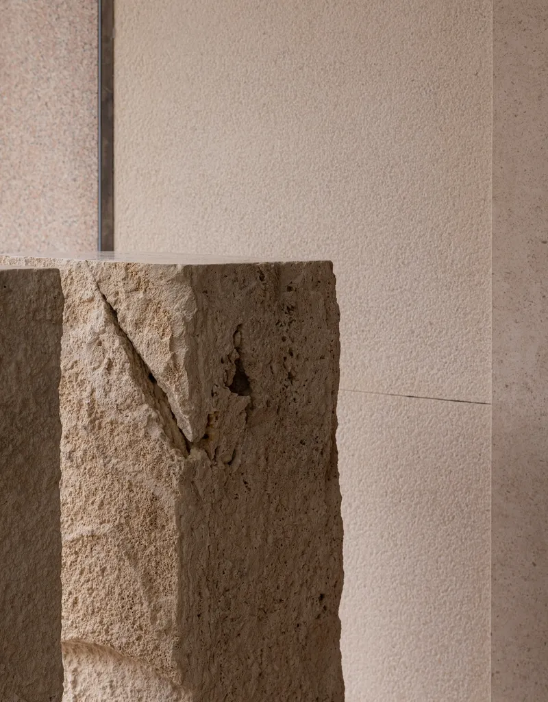 Close-up of rough-cut travertine block meeting smooth limestone wall panel at an interior corner
