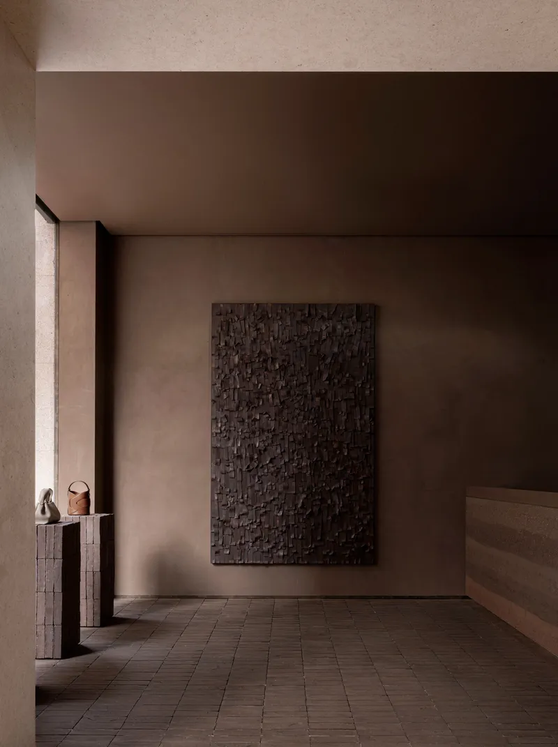 Gallery room with dark textured relief panel on taupe wall and brick tile flooring
