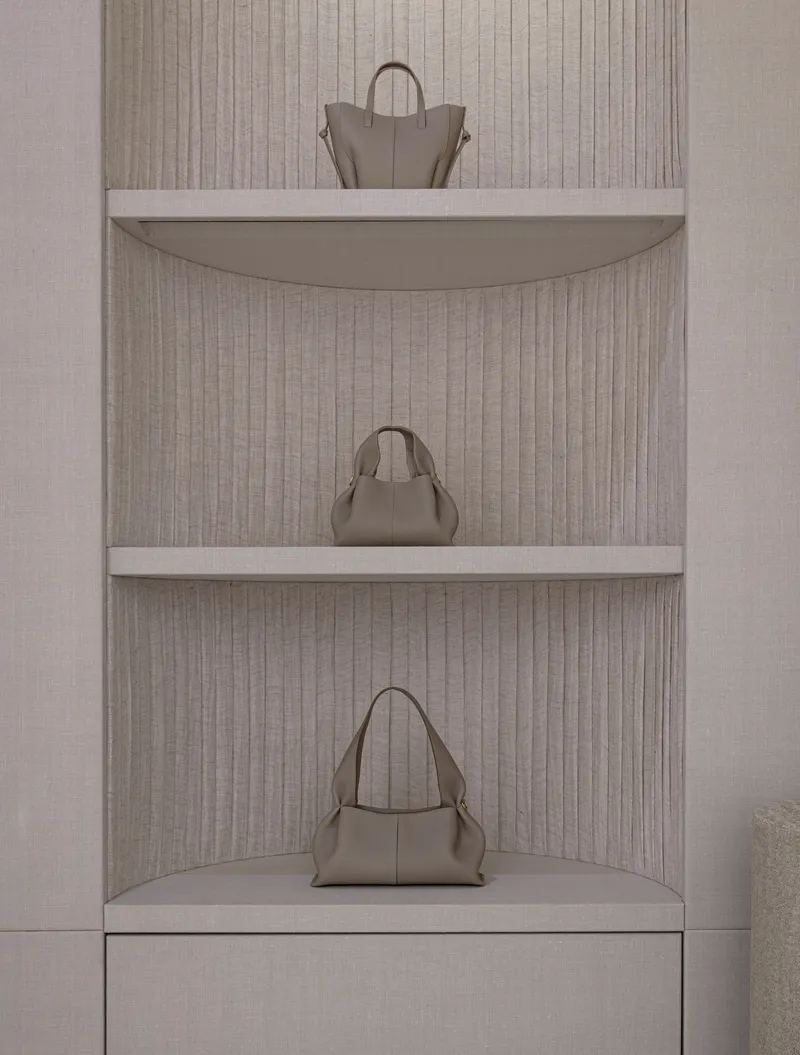 Curved corner shelving niche with fluted linen backing displaying three leather handbags