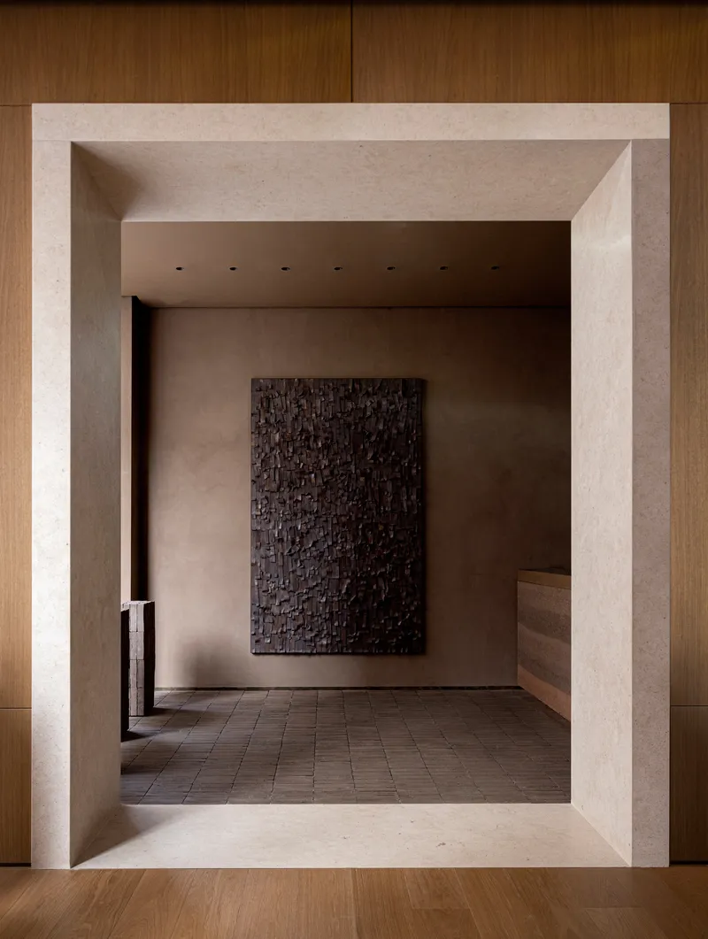 View through beveled stone threshold into a gallery space with textured artwork on rear wall