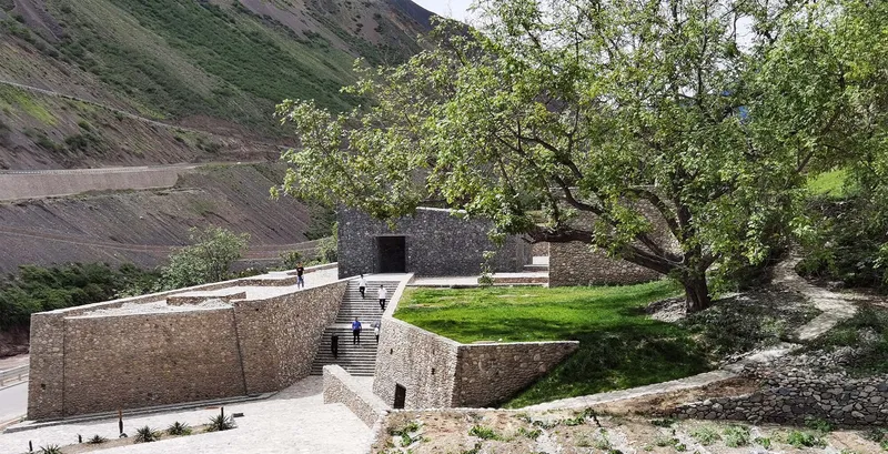 View of the stone walls and lawn terrace framed by a tree against the mountain slope