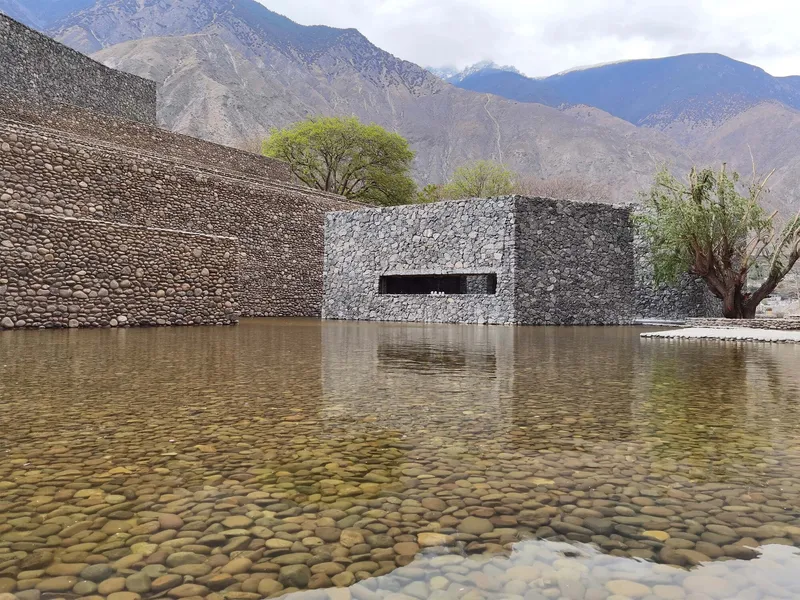 Stone gabion facade reflected in a shallow water pool with mountains in the distance