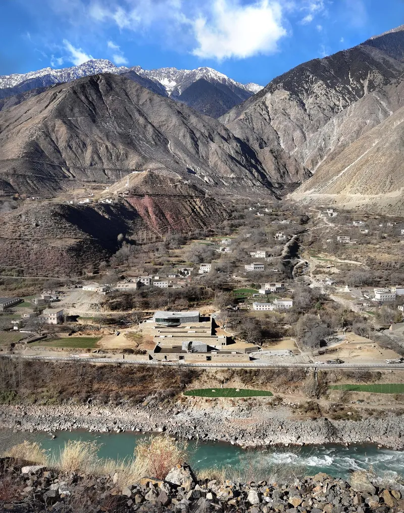 Riverside compound with horizontal stone terraces below snow-capped mountain ridges