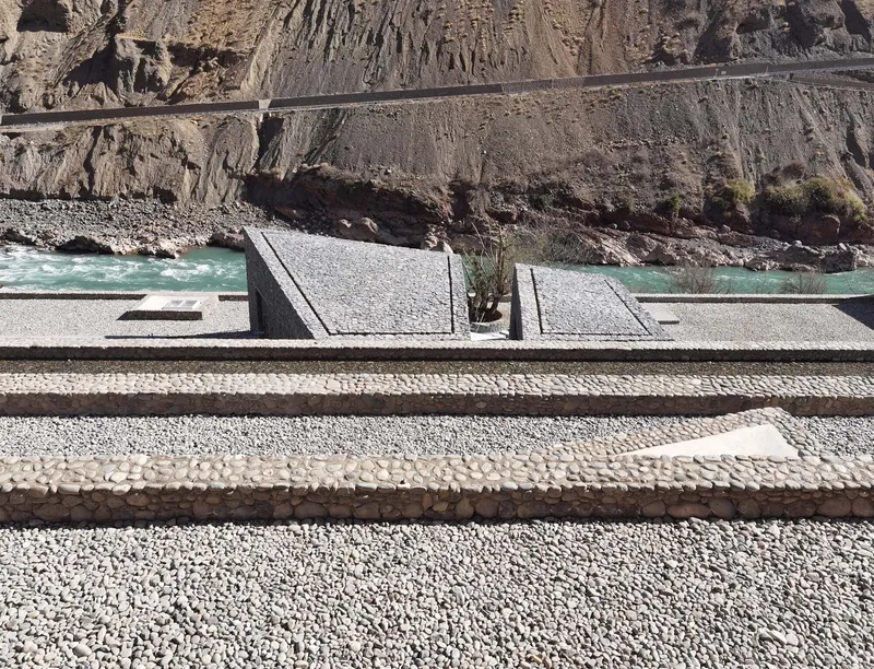 Terraced water basins edged with river stones descending toward a turquoise glacial river below cliffs