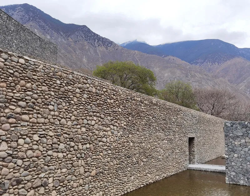 River stone facade with a single recessed doorway set beside a reflecting pool and mountain backdrop