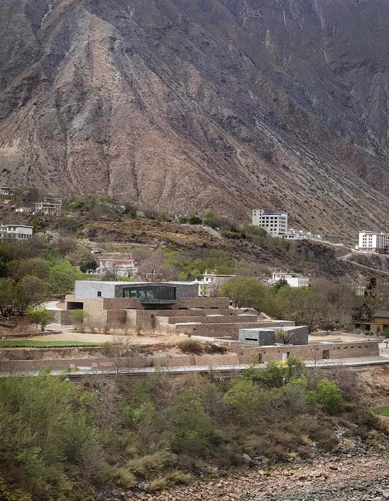 Terraced stone volumes stepping down a hillside against barren mountain slopes with scattered vegetation