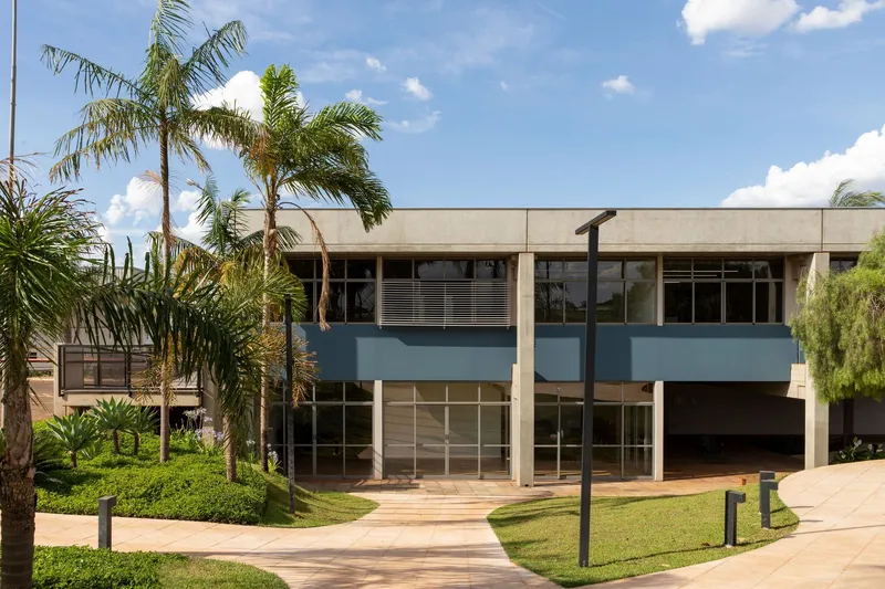 Two-story facade with blue horizontal bands and concrete overhangs framed by palm trees and lawn