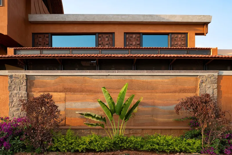 Horizontal banded terracotta wall with stone piers and banana plant against a hedge