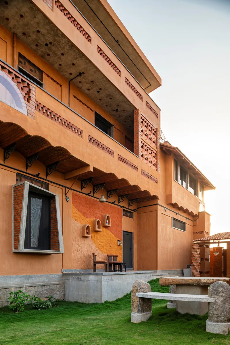 Courtyard facade with overhanging canopy, perforated brick parapet, and concrete seating in grass