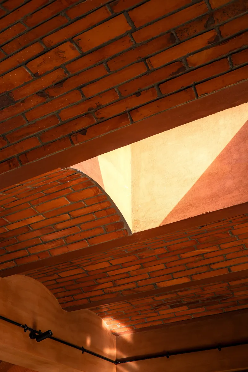 Upward view of curved brick ceiling vaults with warm sunlight streaming through a skylight opening