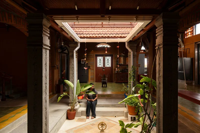 Interior courtyard with stone columns and potted banana plants framing a person standing under tiled skylight