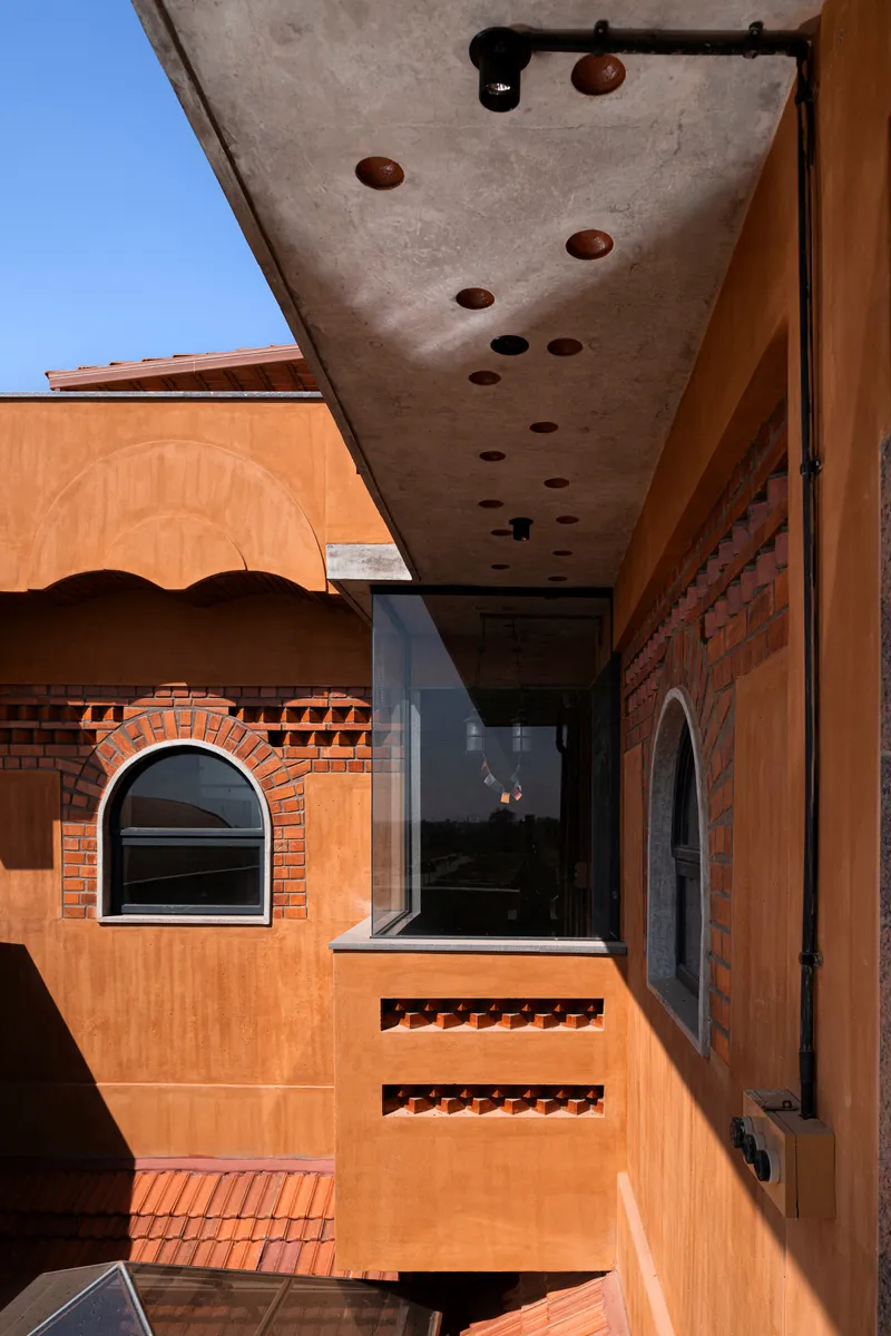 Concrete canopy soffit with circular perforations suspended over a terrace with arched openings below