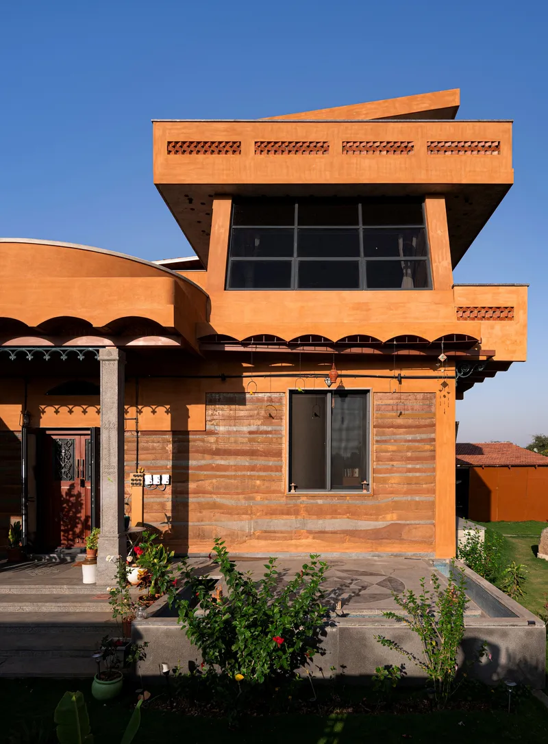 Terracotta brick facade with cantilevered upper volume, scalloped overhangs, and potted plants in afternoon light