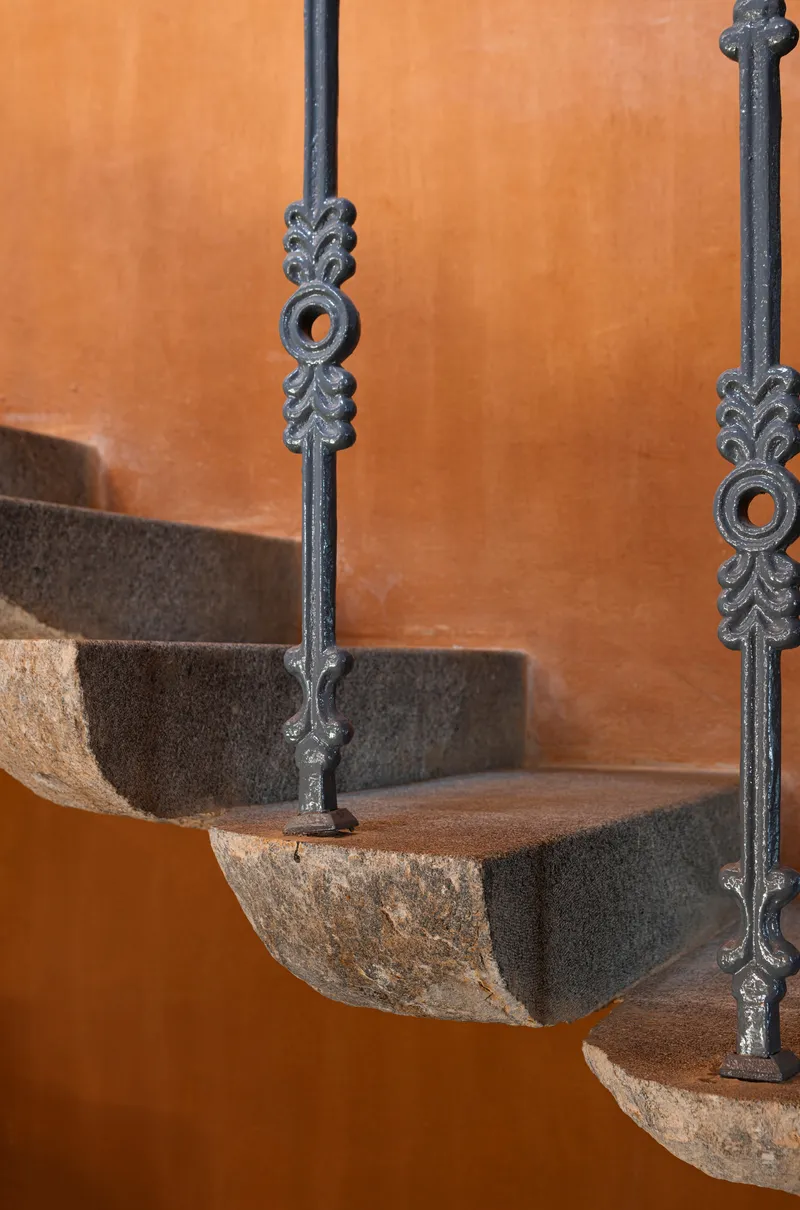 Detail of ornate wrought iron balusters with stone treads against an orange plaster wall