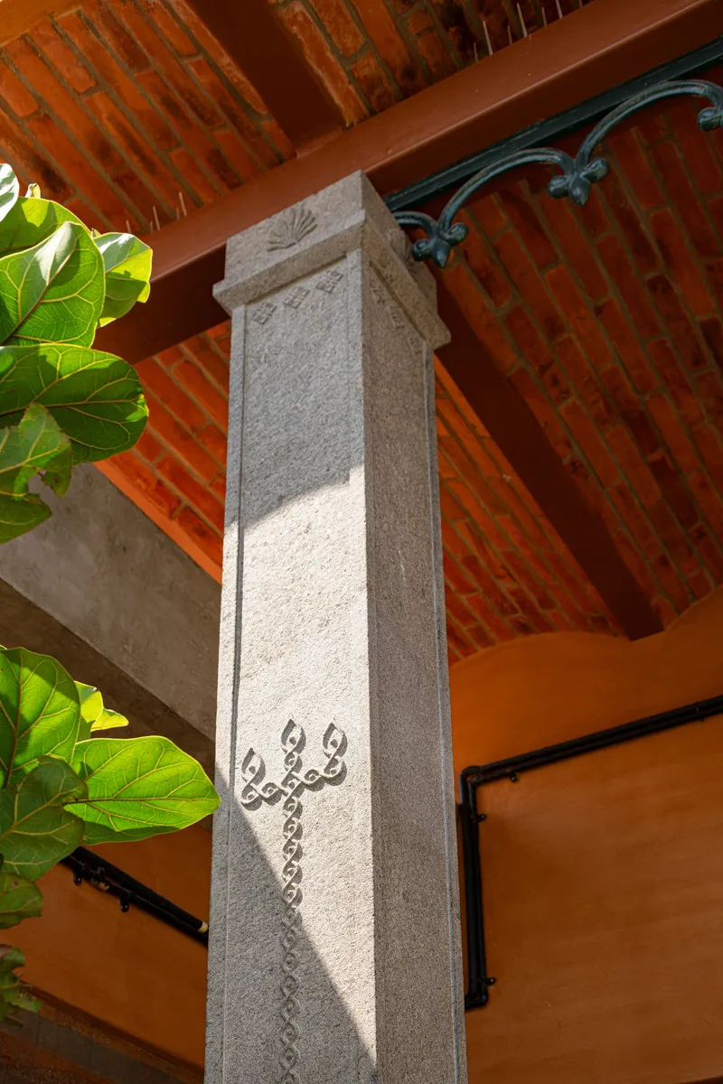 Stone column with carved script detail and wrought iron bracket beneath exposed brick vaulted ceiling