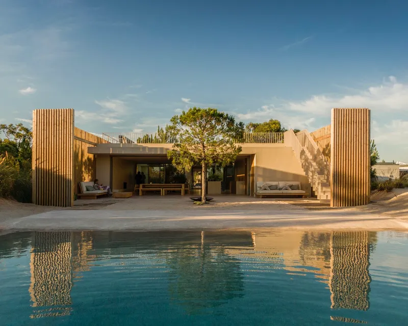 View across the swimming pool toward the timber-slatted facade and terrace in afternoon light