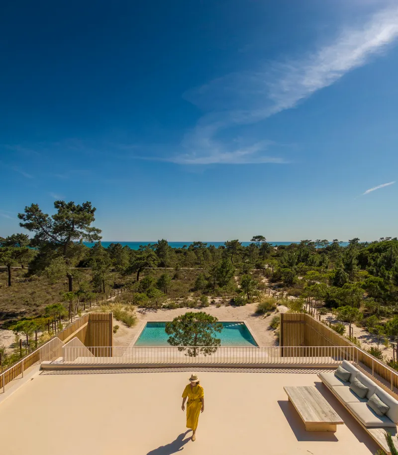 Rooftop terrace overlooking pool and pine forest with a person walking below