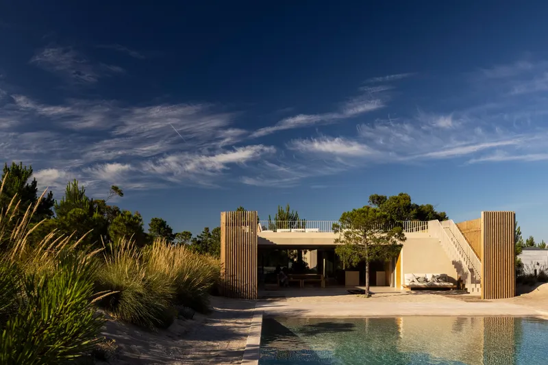 Pool terrace with vertical timber screens flanking a stucco pavilion under wispy cirrus clouds
