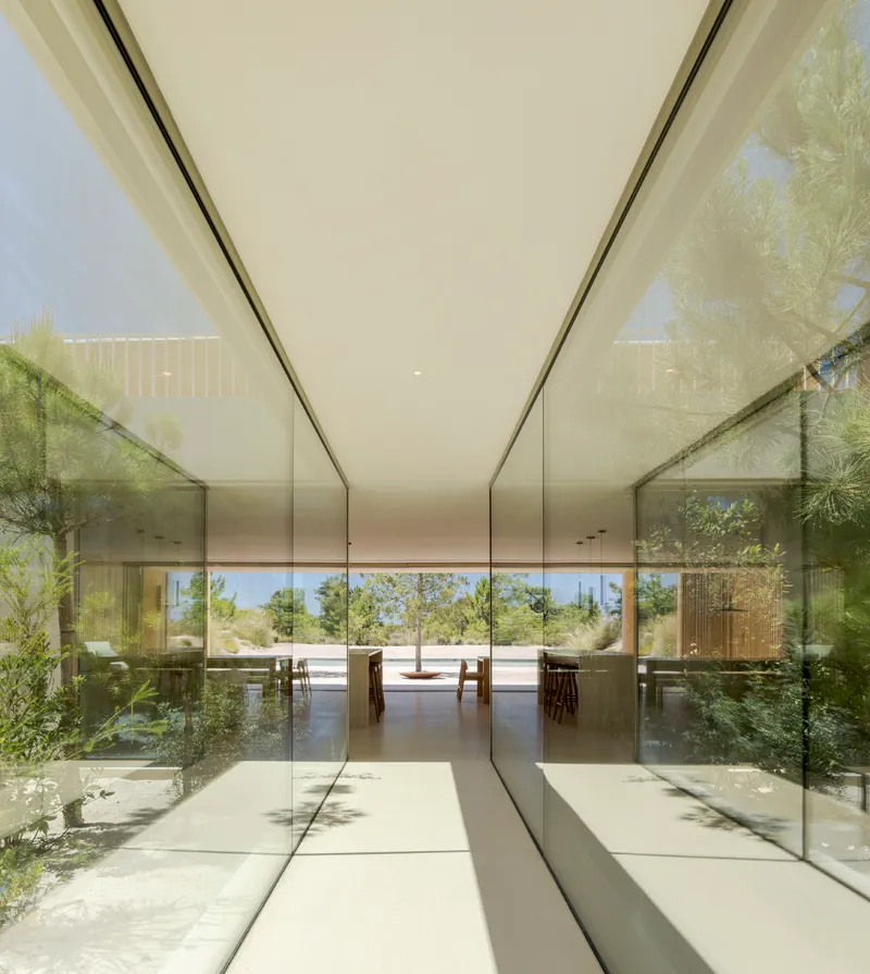 Glass-walled corridor with reflecting polished floor leading to outdoor dunes and grasses