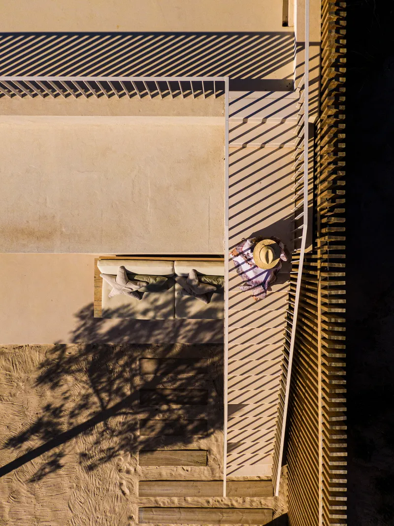 Aerial view of terrace with slatted timber screen casting shadows on pale stone paving and figure seated below