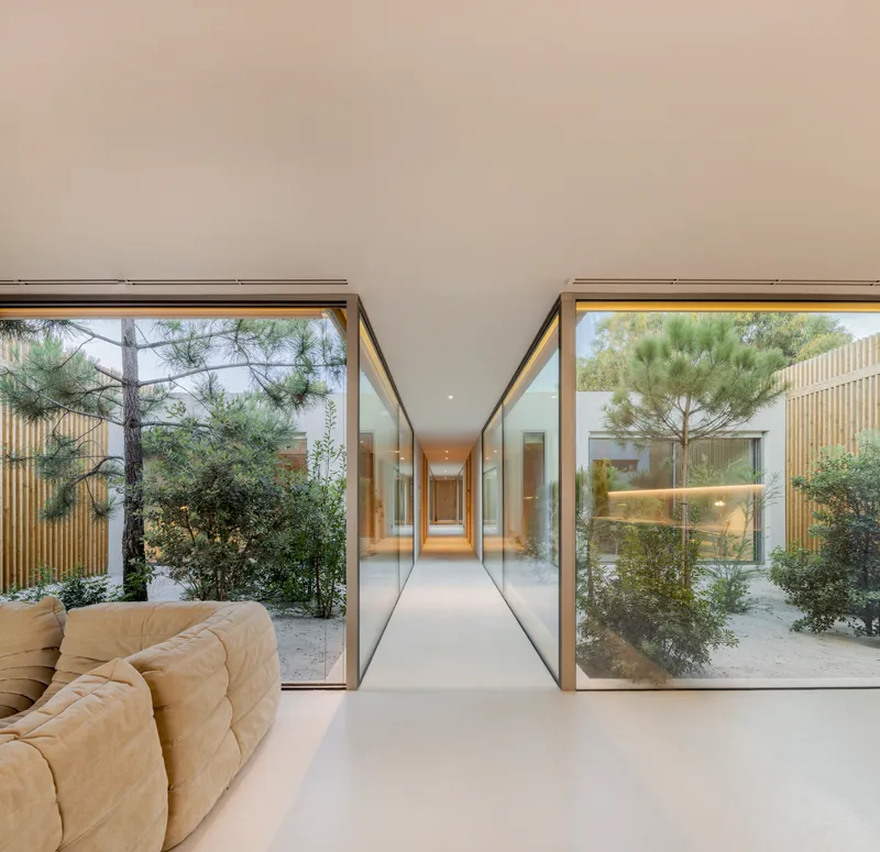 Living space with floor-to-ceiling glass walls opening to planted courtyards on both sides
