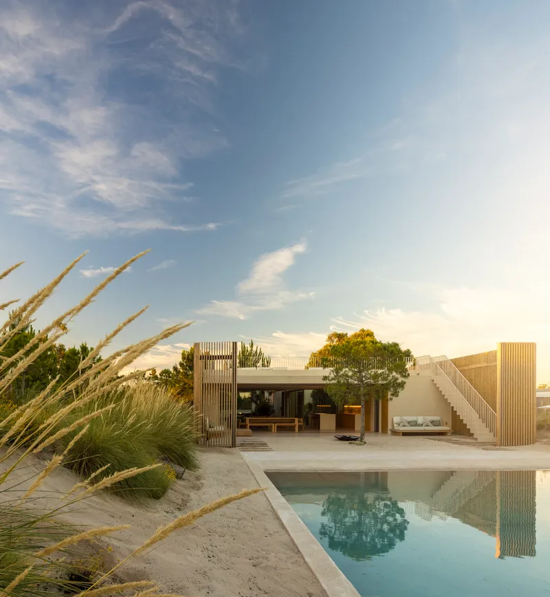 Pool terrace facing timber-clad volumes with outdoor stairs and ornamental grasses at dusk