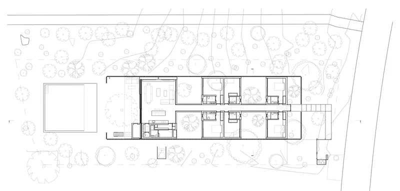 Site plan drawing showing a linear residential volume nestled among trees on sloping terrain