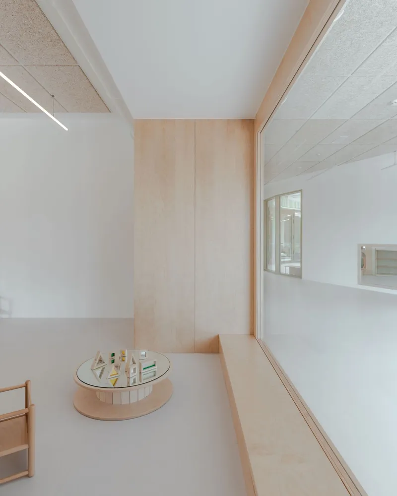 Double-height interior space with pale plywood lining, linear ceiling light, and a circular display table on white flooring