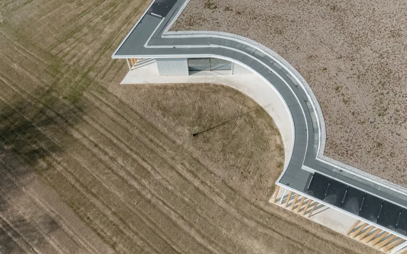 Aerial view of the curved roofline and black asphalt pathway cutting through surrounding agricultural fields
