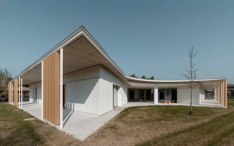 Exterior view showing the gabled and curved roof forms meeting above corrugated walls with a bare tree nearby