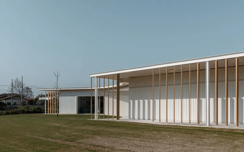 Exterior view of timber colonnade with vertical white metal cladding under an overcast sky