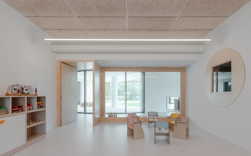 Interior classroom with timber-framed bay window, cork ceiling panels and wooden children's furniture