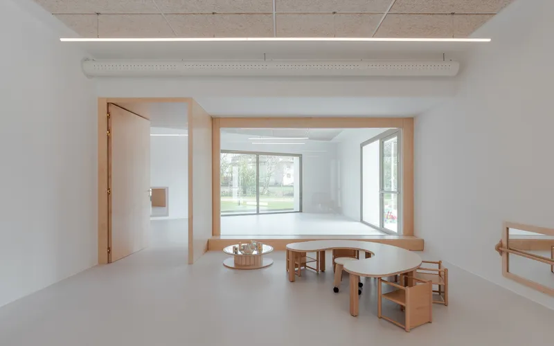 Interior space with timber window seat overlooking the lawn and curved wooden tables on resin flooring