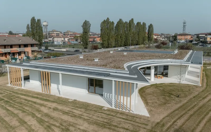 Aerial view of the white single-story structure with green roof and vertical timber screens on open grass