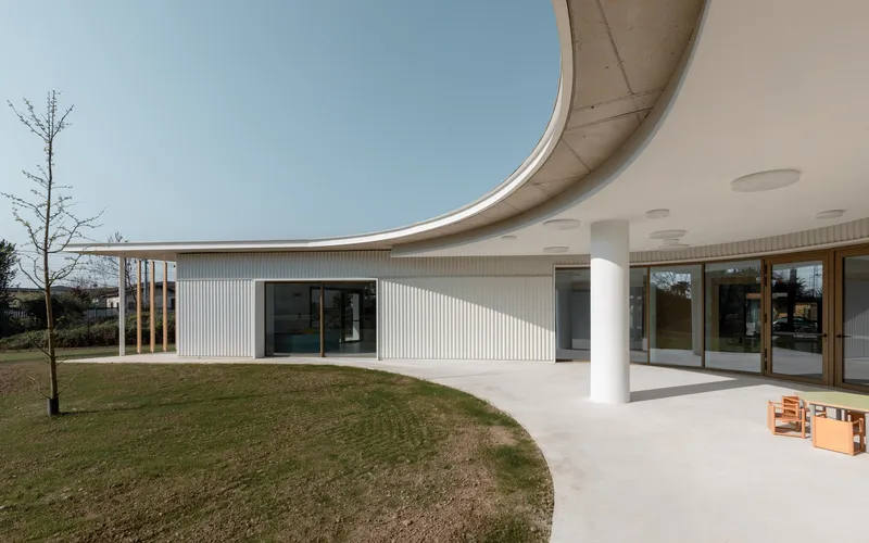 Covered terrace with curved concrete soffit supported by white columns overlooking the lawn