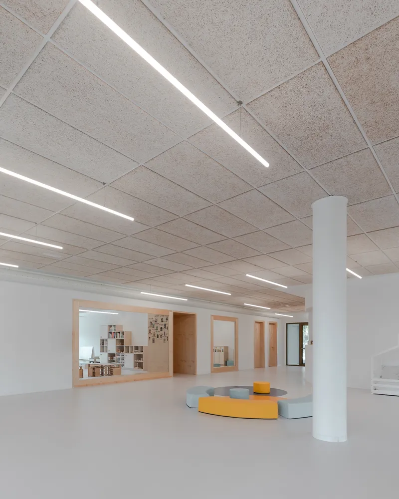 Ceiling with linear light strips in acoustic tile and white circular column beside timber-framed openings