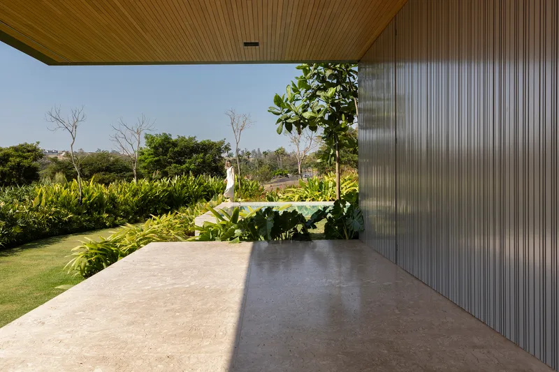 Covered terrace with slatted timber ceiling and corrugated metal wall overlooking planted garden