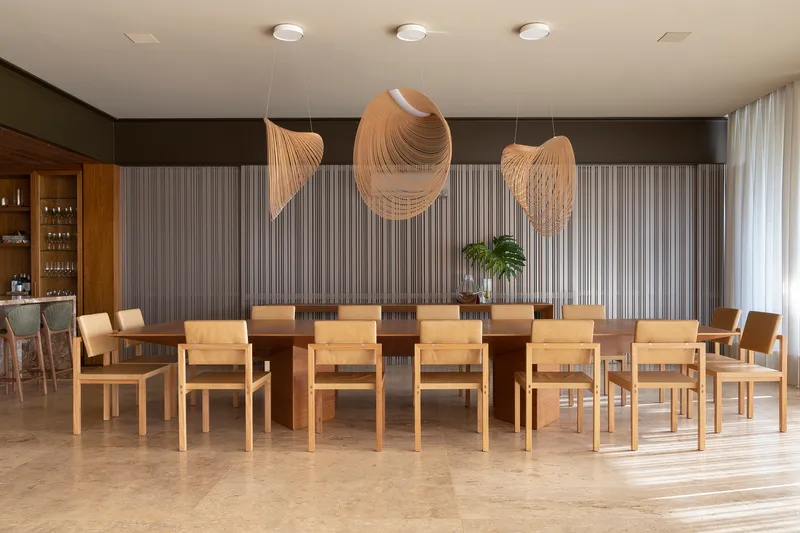 Dining room with long timber table surrounded by light wood chairs beneath sculptural pendant fixtures and vertical paneling