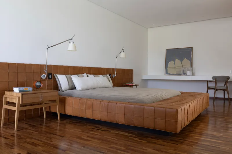 Bedroom featuring a quilted leather headboard and platform bed on dark timber flooring