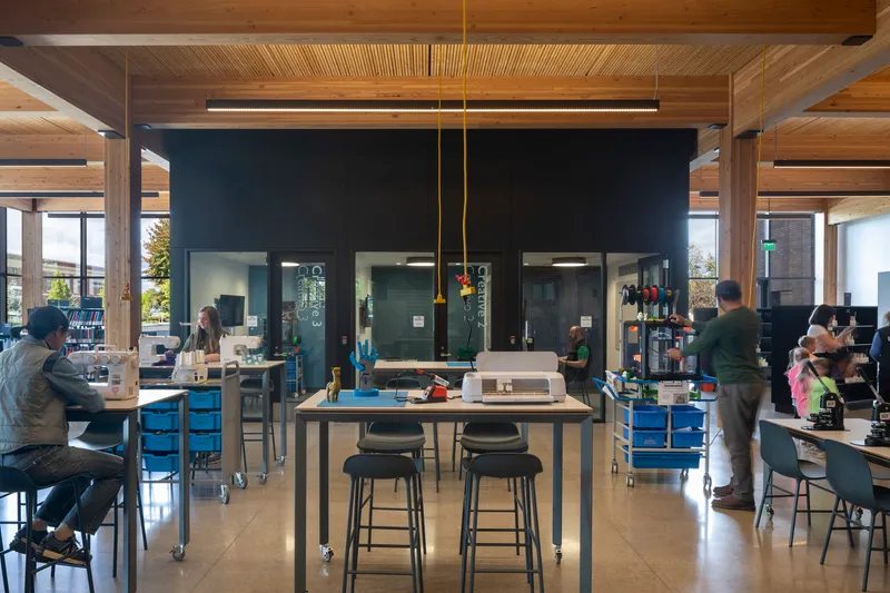 Workshop space with central table, black metal core volume and timber post-and-beam structure under natural light