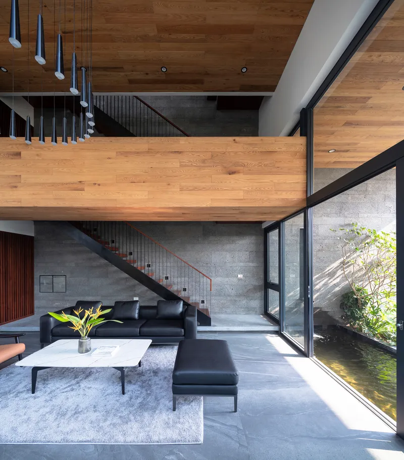 Double-height living room with timber bridge, concrete staircase and glazed wall overlooking interior courtyard pond