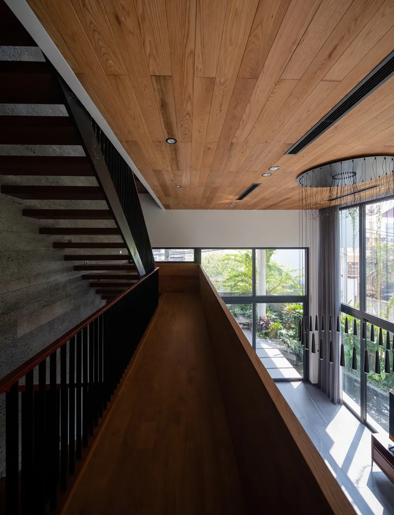 Timber-clad ceiling over hallway landing with open-tread staircase and vertical wood screen filtering daylight