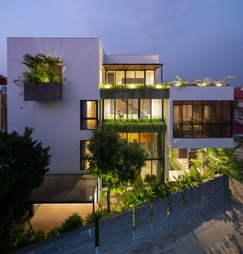 Street facade at twilight showing stacked planted terraces with uplighting and timber screening
