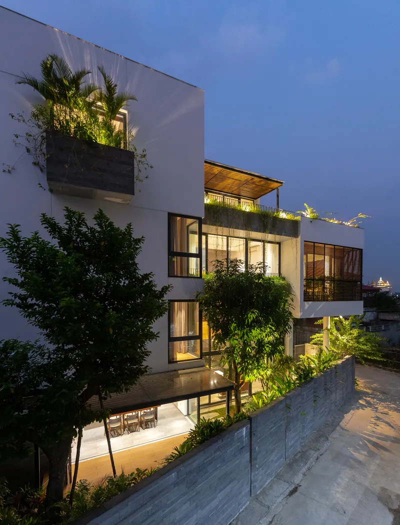 Stepped facade with planted terraces and full-height glazing illuminated at dusk